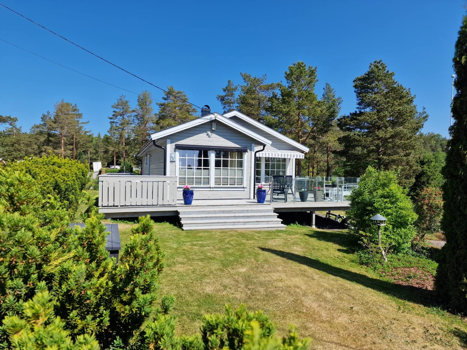 Lys grå hytte med terrasse blant furutrær